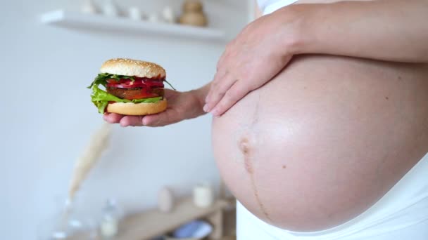 Mujer embarazada sosteniendo hamburguesa. Anhelos de comida chatarra para el embarazo. Primer plano. . — Vídeos de Stock