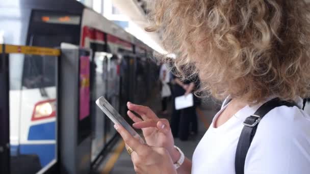 Женщина с помощью смартфона на платформе метро ждет поезда — стоковое видео