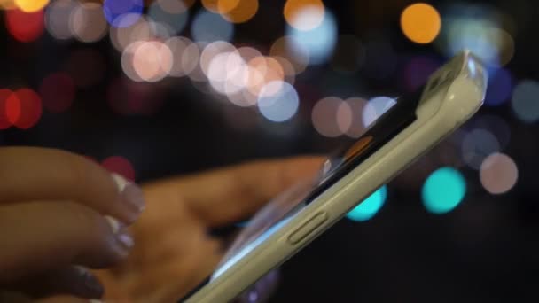 As mãos da mulher usando telefone inteligente com luz noturna Bokeh fundo — Vídeo de Stock