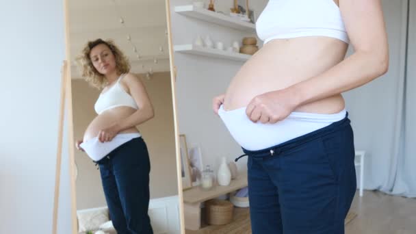 Clothes For Pregnant Women. Woman In Blue Trousers With High Waist Looking In Mirror. — Stock Video