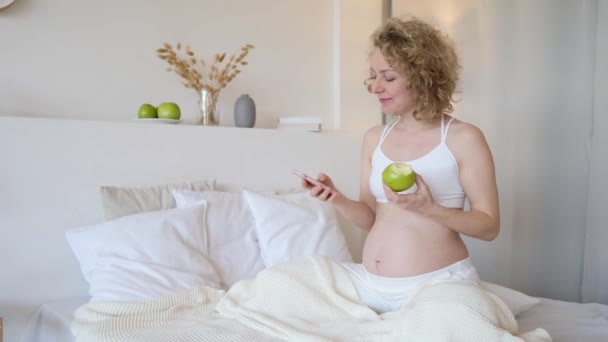 Schöne schwangere Frau benutzt Handy in ihrem Schlafzimmer — Stockvideo