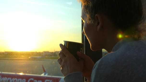 Жінка з кавою очікування в залі вильоту в аеропорту на заході сонця — стокове відео
