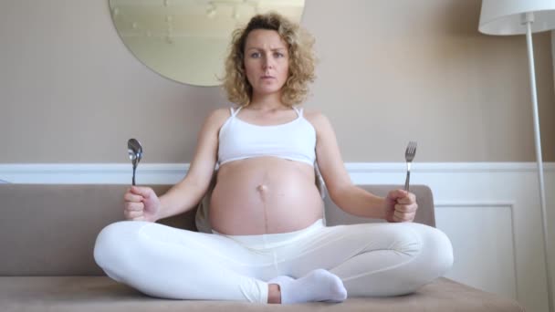 Hambrienta mujer embarazada insatisfecha sosteniendo cuchara y tenedor en las manos esperando comida . — Vídeos de Stock