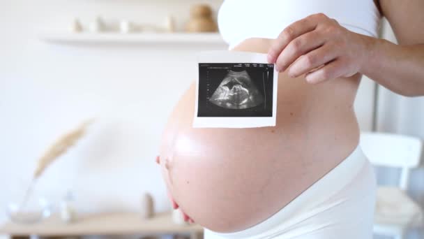 Zwangere vrouw houdt echografie foto op haar buik — Stockvideo