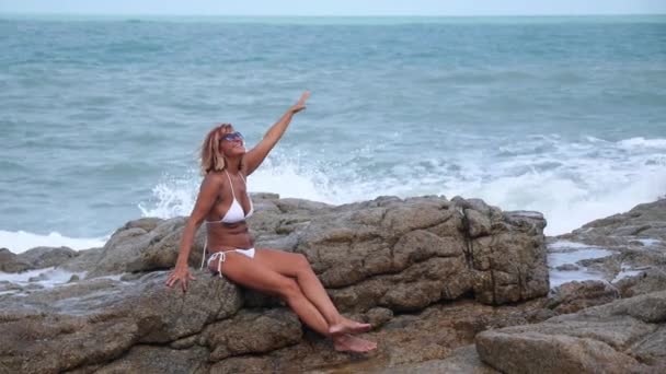 Estilo de vida: Mujer mayor en bikini sentada en piedra por mar — Vídeos de Stock