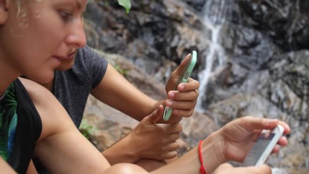 Twee wandelaars toeristische vrouwen met behulp van mobiele telefoon bij Waterval — Stockvideo