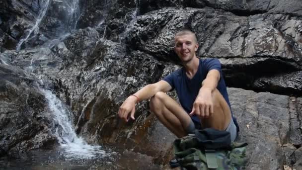 Юный спортсмен у водопада с поднятыми вверх пальцами после похода — стоковое видео