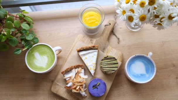 Draufsicht auf trendige pflanzliche Lebensmittel - blauer Matcha-Latte und vegane Kuchen. — Stockvideo