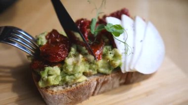 Avokado tostunu çatal ve bıçakla kesiyorum. Yakın plan.