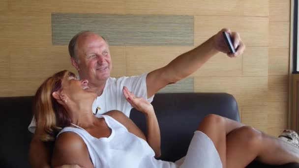 Pareja mayor sentada en sofá tomando selfie — Vídeos de Stock