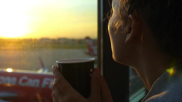 Женщина-путешественница в аэропорту пьет кофе и смотрит на самолет — стоковое видео