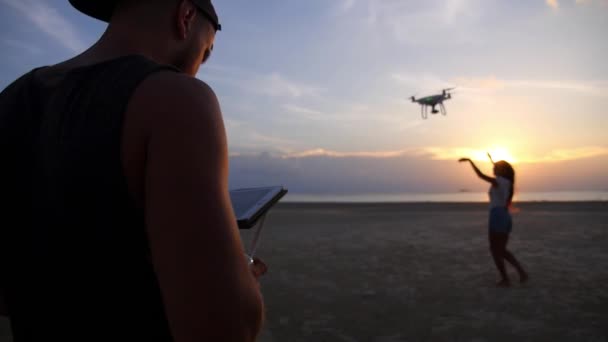 Mann mit fliegender Drohne mit Fernbedienung am Strand bei Sonnenuntergang — Stockvideo