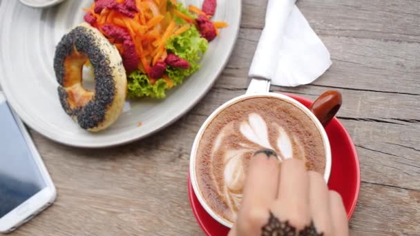 Mano agita el café en la taza en la tabla de madera con el teléfono elegante y la comida — Vídeos de Stock