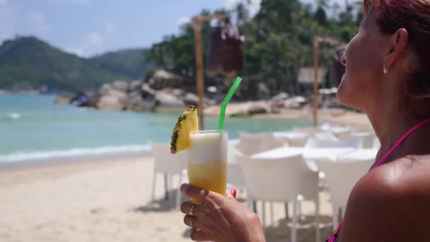 Feliz mujer mayor bebiendo cóctel tropical en la playa mirando al mar — Vídeos de Stock