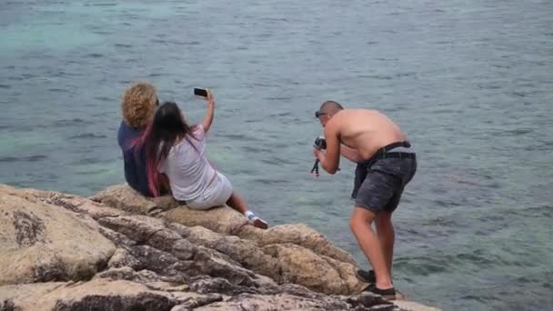 Videógrafo Hombre Dispara Un Vídeo De Dos Chicas Haciendo Selfie Junto Al Mar — Vídeos de Stock