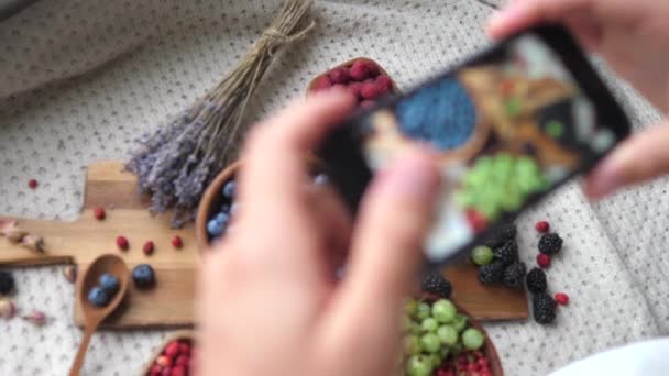 Las manos tomando fotos de alimentos saludables usando Smartphone. Mezclar bayas en la mesa . — Vídeos de Stock