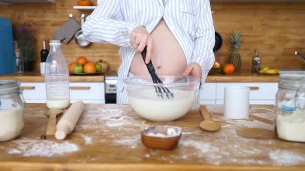 Mujer embarazada azotando la leche en un tazón mientras cocina en la cocina . — Vídeos de Stock