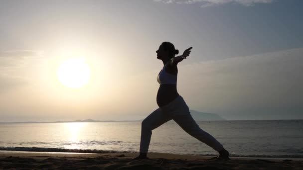 Hamile kadın gün doğumunda sahilde yoga yapıyor.. — Stok video