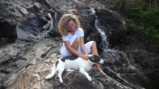 Junge Frau sitzt mit ihrem Hund am Wasserfall — Stockvideo