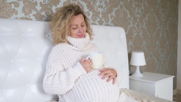 Boldog terhességet, a terhes nő életmódját kötött pulóverben pihentető kényelmes ágyban. — Stock videók