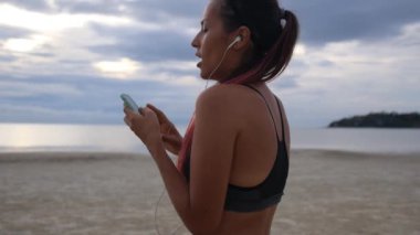 Koşudan sonra sahilde akıllı telefon egzersizleri yapan spor kadını.