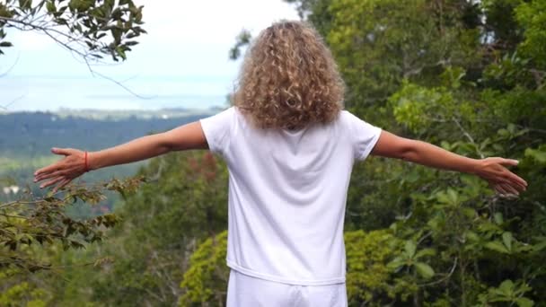 Девушка в белой одежде, расправляющая руки на вершине горы — стоковое видео