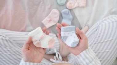 Bir erkek ve bir kız için bebek çorabı tutan hamile bir kadın..