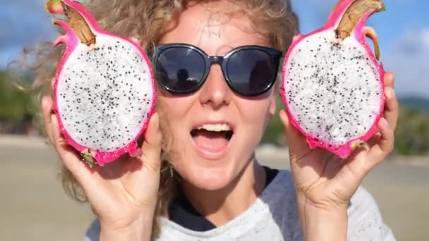 Jonge vrouw met draak pitaya fruit ogen op het strand — Stockvideo