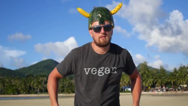 Man met bananengeweer in Vegan T-Shirt en Viking Fruit Helm op het strand — Stockvideo