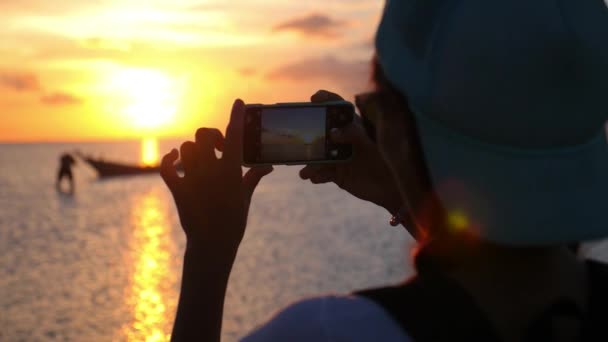 Kvinnan tar bilder med smartphone vid solnedgången över havet — Stockvideo