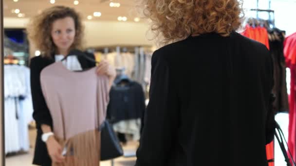 Mujer comprando ropa mirando en espejo en tienda de ropa — Vídeos de Stock