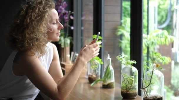 Молодая улыбающаяся женщина с помощью мобильного телефона в кафе — стоковое видео