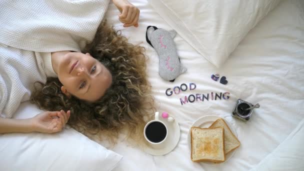 Bir kadın kahvaltıda kahve ve tostla yatakta uzanıyor. Günaydın konsept.. — Stok video
