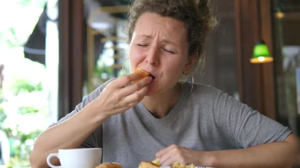 Смешная девушка ест кондитерские изделия и плачет в кафе — стоковое видео