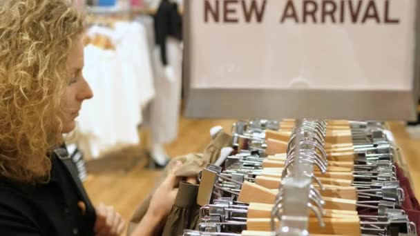 Vrouw op zoek naar kleding tijdens het winkelen in de kledingwinkel — Stockvideo