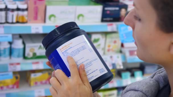 Femme lisant l'étiquette sur le supplément de poudre de protéine en pharmacie — Video