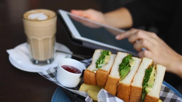 Las manos femeninas usando la tableta durante el desayuno con café y sándwich . — Vídeo de stock