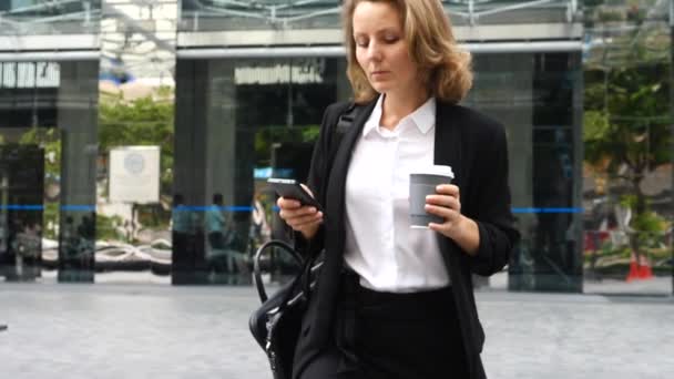 İş kadını Ofis binasında elinde kahve fincanıyla akıllı telefon kullanıyor. — Stok video