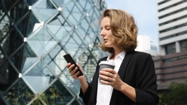 Jonge zakenvrouw met koffie te gaan met behulp van mobiele telefoon — Stockvideo