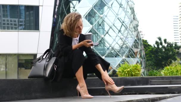Бизнесмен отдыхает с кофе на открытом воздухе, чувствуя боль после ношения высоких каблуков — стоковое видео