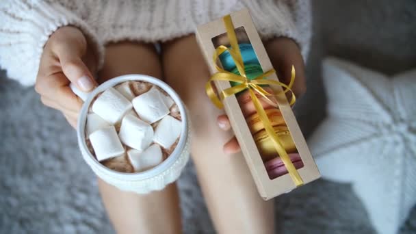 Manos sosteniendo la taza de chocolate caliente con malvaviscos y macarrones caja de regalo — Vídeos de Stock