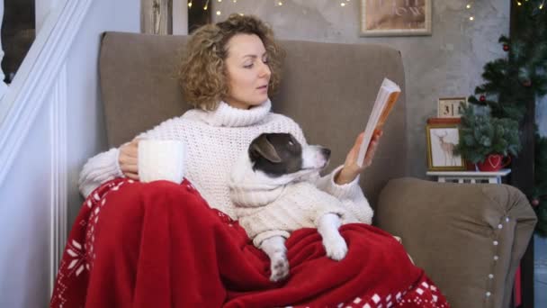 Frau liest Buch mit Hund zu Weihnachten zu Hause. — Stockvideo