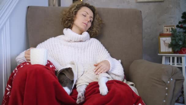 Ung kvinna och hund sover på stol hemma. Mysig vinter semester koncept. — Stockvideo