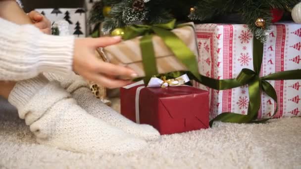 Piernas femeninas en calcetines sentadas cerca del árbol de Navidad con cajas de regalo — Vídeo de stock