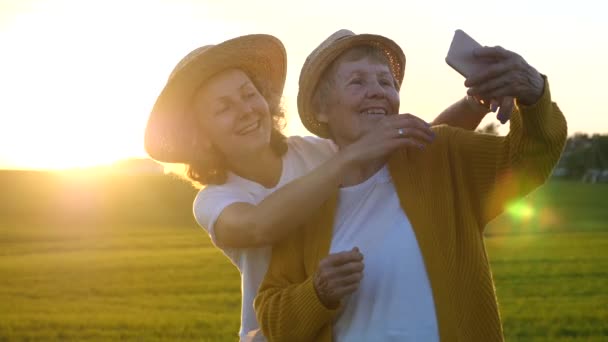 Mutlu yaşlı büyükanne, akıllı telefonuyla gün batımında torunuyla selfie çekiyor. — Stok video