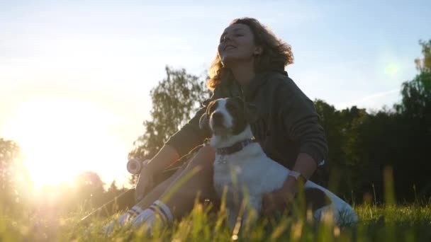 Flicka sitter utomhus med hund i parken vid solnedgången — Stockvideo