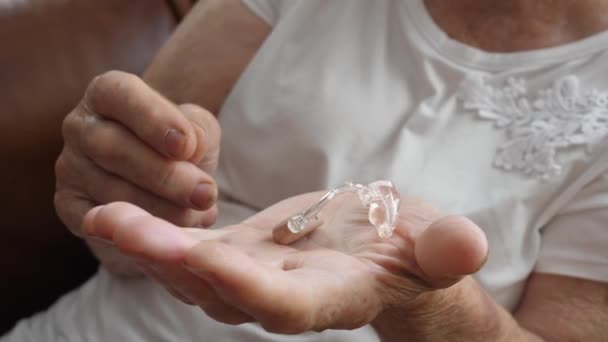 Handen van een oudere vrouw die een gehoorapparaat vasthoudt. Sluitingsdatum. — Stockvideo