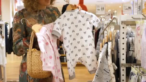 Покупательница выбирает одежду для ребенка в магазине детской одежды — стоковое видео