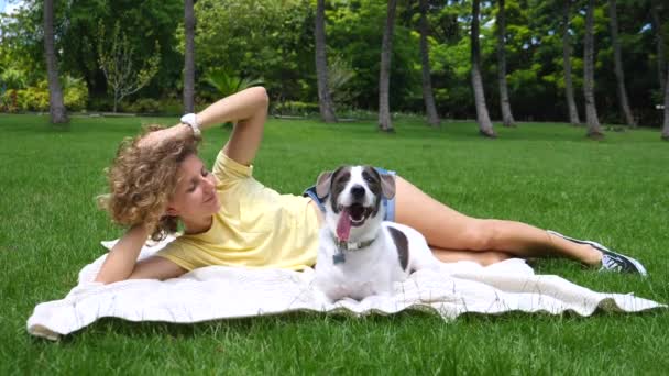 Meisje ontspannen met hond buiten liggend op groen gras in de zomer — Stockvideo