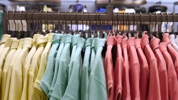 Красочные футболки с поло отображаются на вешалках в магазине одежды. Закрытие . — стоковое видео